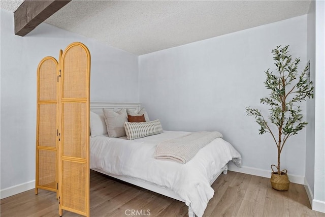 bedroom with a textured ceiling, light hardwood / wood-style flooring, and beam ceiling