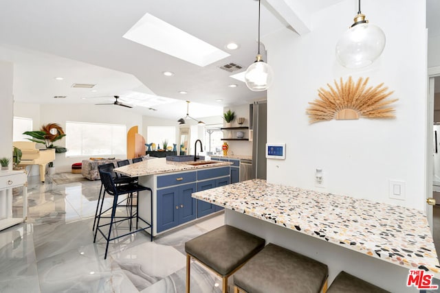 kitchen featuring ceiling fan, sink, hanging light fixtures, blue cabinets, and a kitchen bar