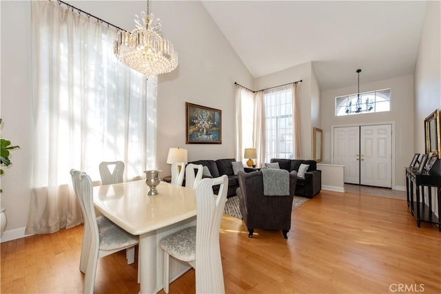 dining space with light wood-type flooring, high vaulted ceiling, and a chandelier