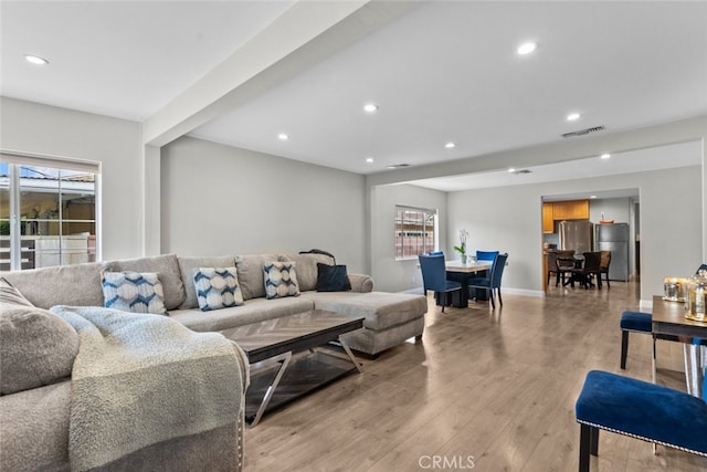 living room featuring beamed ceiling, light wood-type flooring, and a wealth of natural light