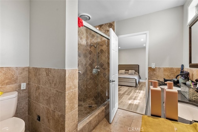 bathroom featuring tile patterned floors, a shower with shower door, tile walls, and toilet