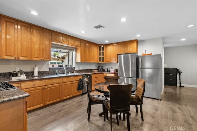 kitchen with appliances with stainless steel finishes, light hardwood / wood-style flooring, dark stone counters, and sink