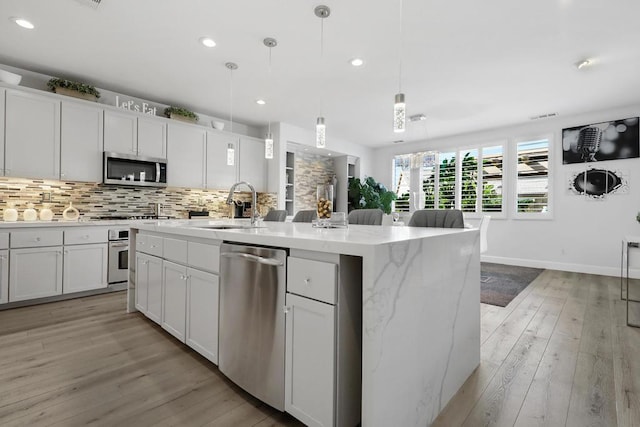 kitchen with pendant lighting, sink, white cabinetry, stainless steel appliances, and an island with sink