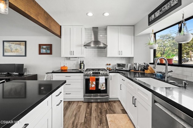 kitchen featuring appliances with stainless steel finishes, dark hardwood / wood-style flooring, wall chimney exhaust hood, sink, and white cabinets