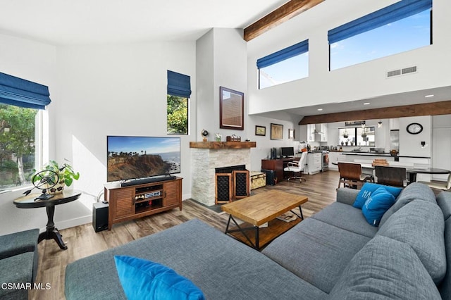 living room featuring a stone fireplace, light hardwood / wood-style flooring, high vaulted ceiling, and beamed ceiling