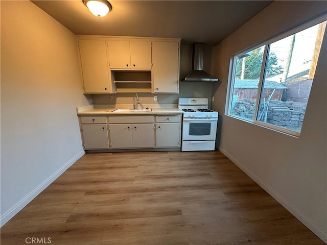 kitchen with light hardwood / wood-style floors, wall chimney range hood, sink, and white range with gas cooktop