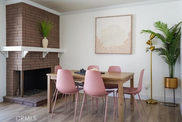 dining area with crown molding, wood-type flooring, and a brick fireplace