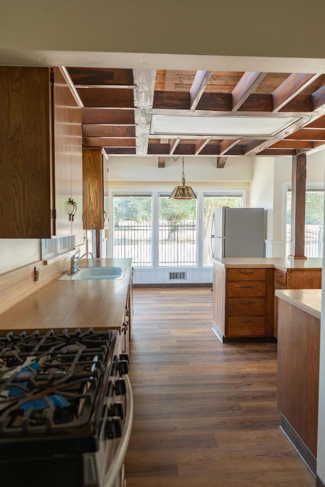 kitchen featuring gas range, stainless steel refrigerator, sink, dark hardwood / wood-style flooring, and pendant lighting