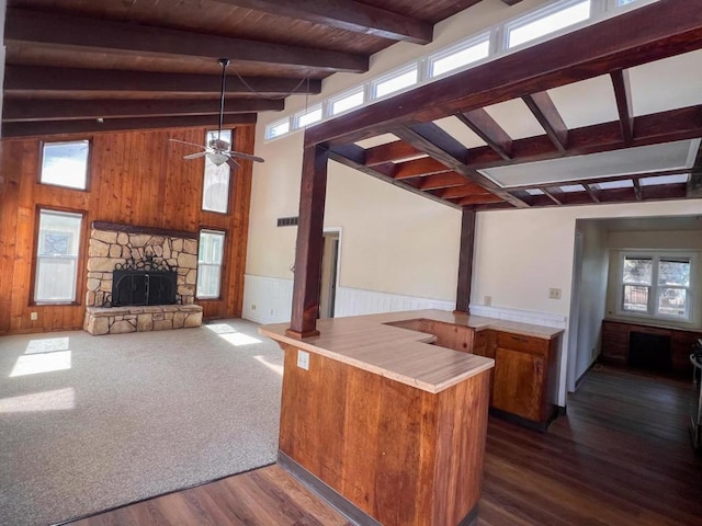 kitchen with a stone fireplace, vaulted ceiling with beams, dark hardwood / wood-style floors, ceiling fan, and kitchen peninsula