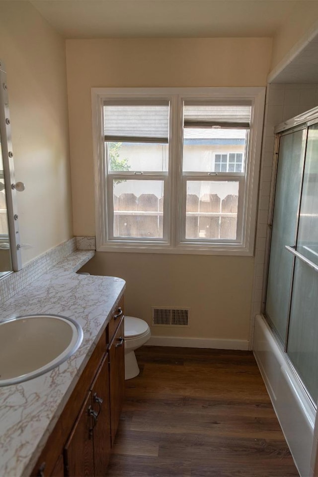 full bathroom featuring hardwood / wood-style floors, vanity, combined bath / shower with glass door, and toilet