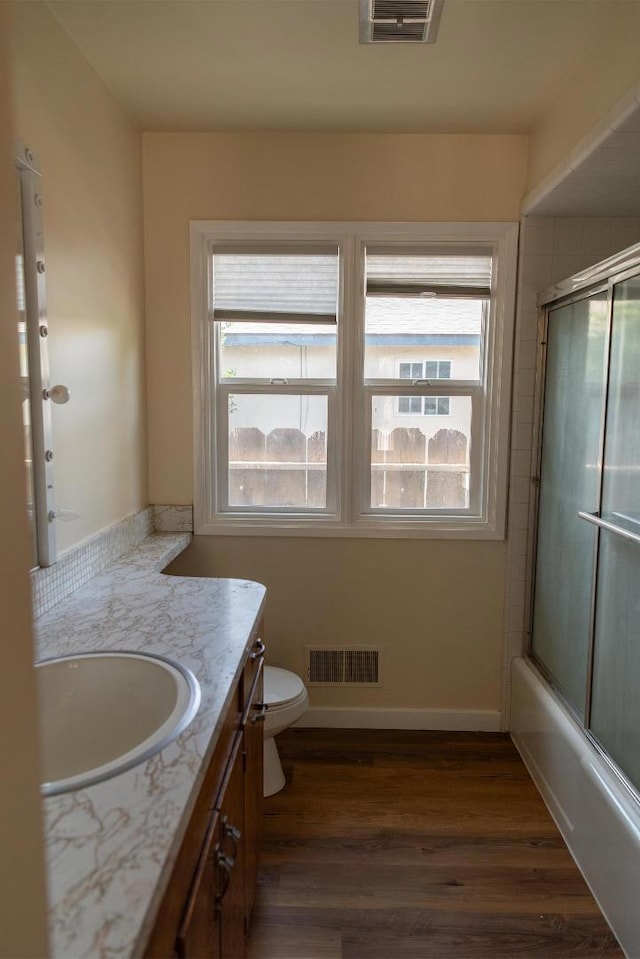 full bathroom featuring hardwood / wood-style floors, vanity, combined bath / shower with glass door, and toilet