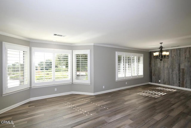 empty room featuring a notable chandelier, crown molding, dark wood-type flooring, and wooden walls