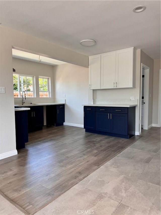 kitchen with white cabinets, sink, blue cabinetry, and light hardwood / wood-style flooring