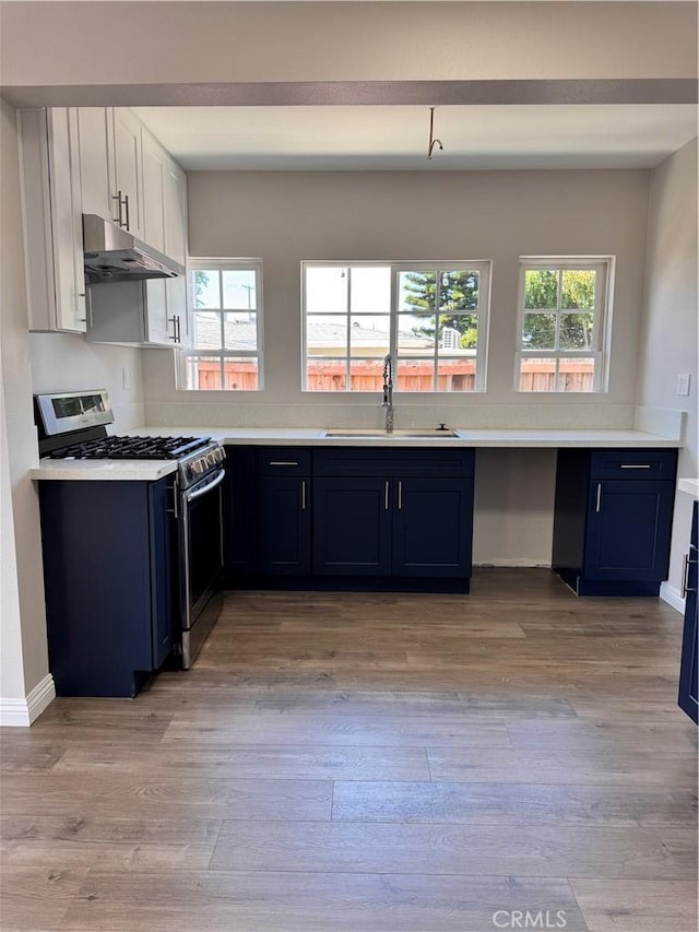 kitchen featuring stainless steel gas range, blue cabinets, sink, white cabinets, and light hardwood / wood-style floors