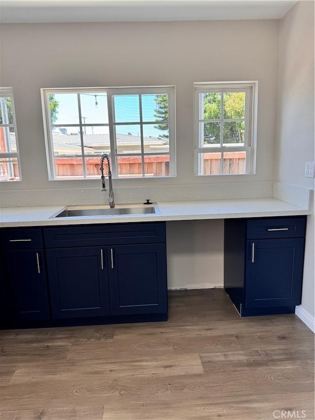 kitchen featuring blue cabinetry, a healthy amount of sunlight, sink, and light hardwood / wood-style flooring