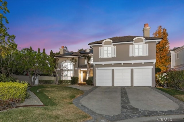 view of front of house featuring a garage, a lawn, solar panels, concrete driveway, and stucco siding