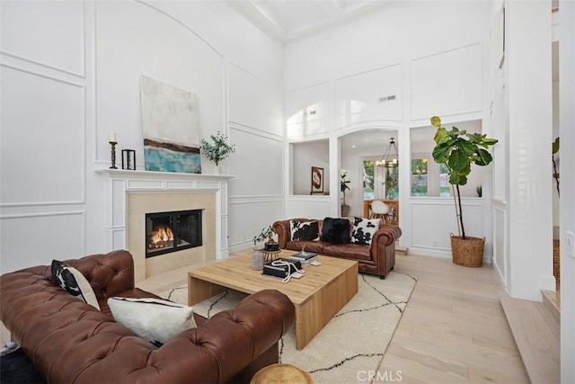 living room with a notable chandelier, visible vents, a decorative wall, a premium fireplace, and light wood-type flooring