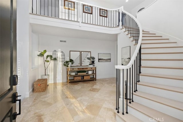 foyer featuring visible vents, stairway, a towering ceiling, and baseboards