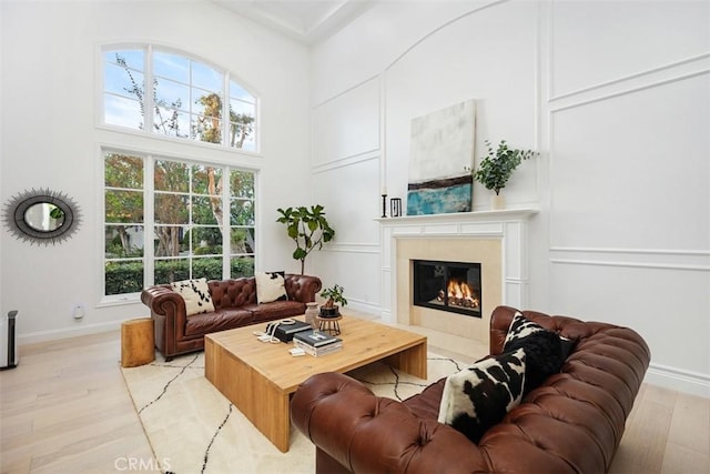 living room with a fireplace, a decorative wall, light wood-style flooring, and a towering ceiling