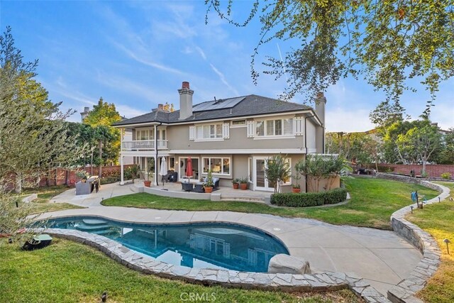 back of house with a lawn, solar panels, a balcony, a fenced in pool, and a patio area