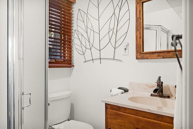 bathroom with a shower with door, vanity, and toilet