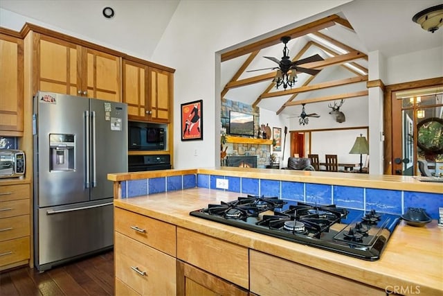 kitchen with wood counters, black appliances, dark hardwood / wood-style floors, a stone fireplace, and lofted ceiling