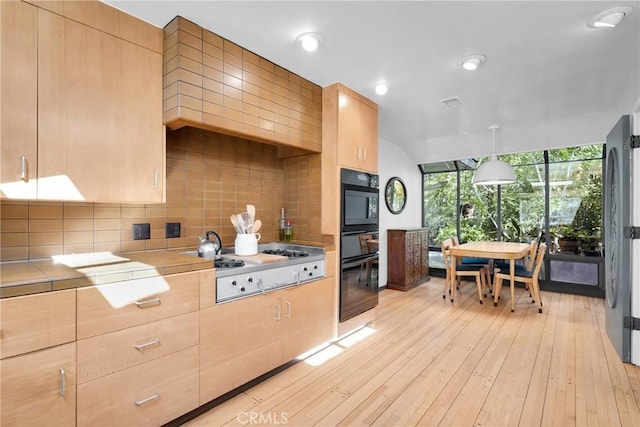 kitchen with tasteful backsplash, black appliances, light brown cabinets, light hardwood / wood-style flooring, and hanging light fixtures