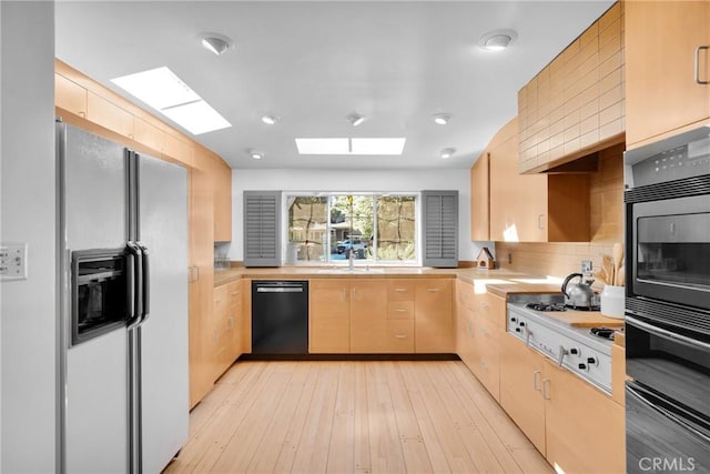 kitchen with a skylight, tasteful backsplash, black appliances, light brown cabinets, and light hardwood / wood-style flooring