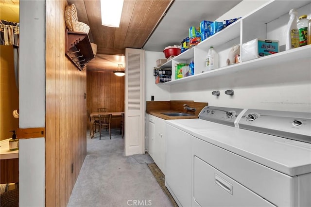 laundry area with wood walls, cabinets, wooden ceiling, sink, and washing machine and clothes dryer