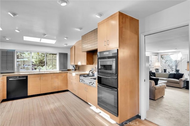 kitchen with a skylight, light brown cabinets, light hardwood / wood-style flooring, backsplash, and black appliances