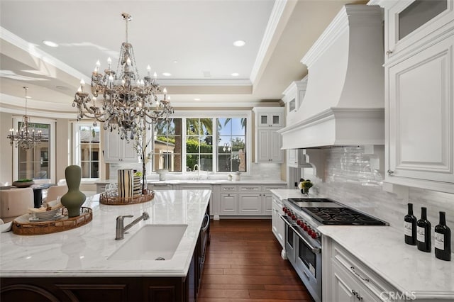 kitchen featuring light stone countertops, backsplash, sink, range with two ovens, and white cabinetry