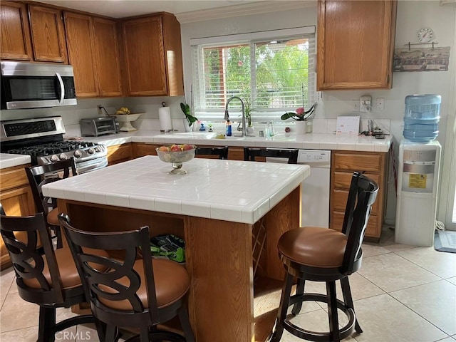 kitchen with a breakfast bar, crown molding, light tile patterned floors, tile counters, and stainless steel appliances