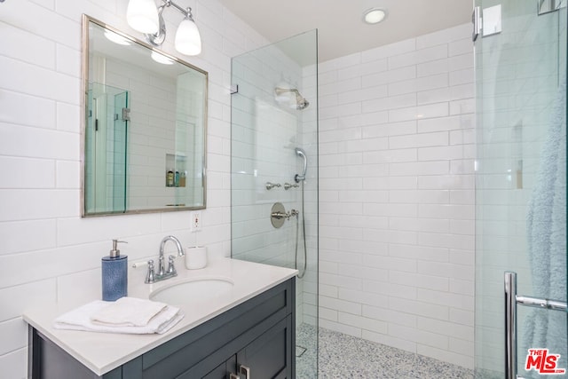 bathroom with vanity, backsplash, a shower with door, and tile walls