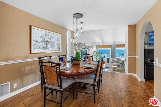 dining room with wood-type flooring, vaulted ceiling with beams, and a water view