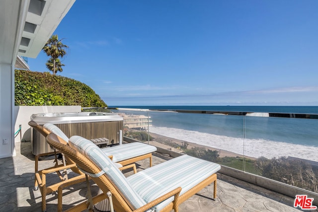 view of patio / terrace featuring a water view, a hot tub, and a view of the beach