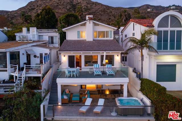 rear view of house featuring a mountain view, a balcony, and a hot tub