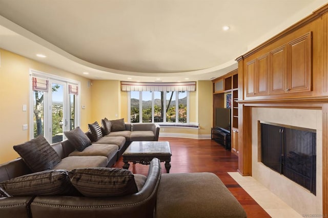 living room featuring a raised ceiling, a tile fireplace, and dark wood-type flooring