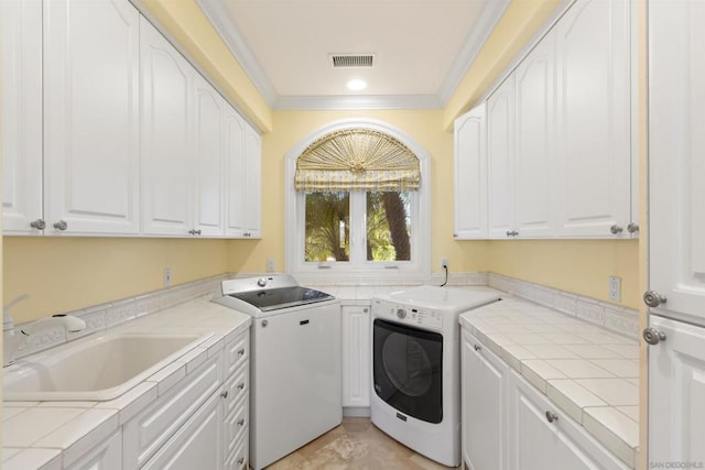 laundry room featuring washer and dryer, cabinets, ornamental molding, and sink