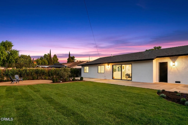 back house at dusk with a lawn and a patio area