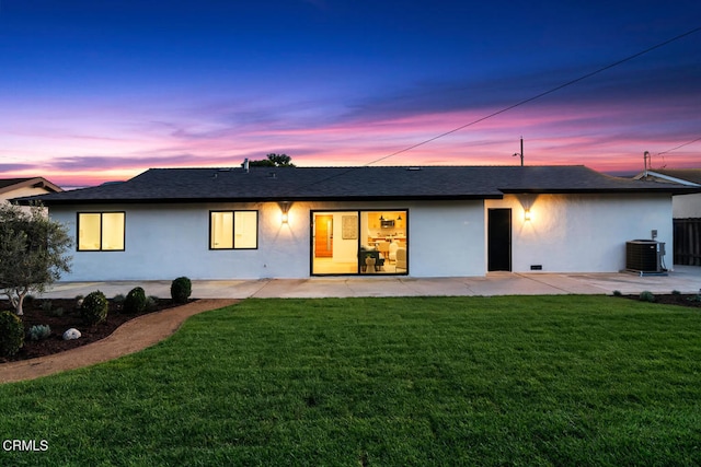 back house at dusk with a lawn, central air condition unit, and a patio