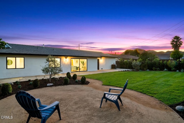 back house at dusk featuring a patio, cooling unit, and a lawn