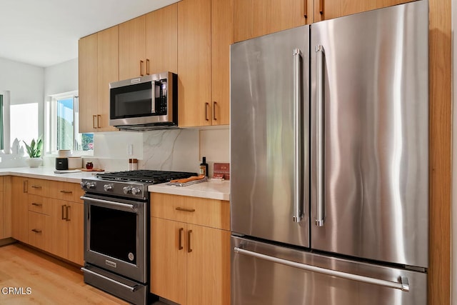 kitchen featuring decorative backsplash, light brown cabinets, stainless steel appliances, and light hardwood / wood-style flooring