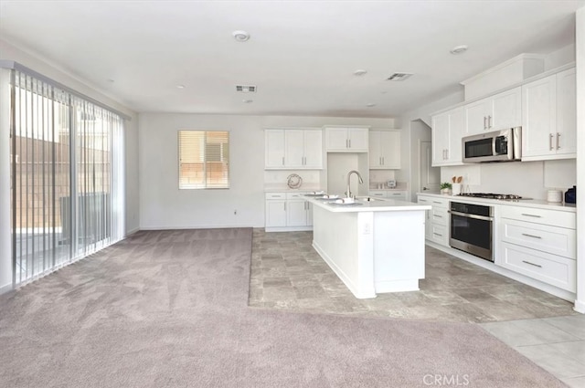 kitchen featuring a kitchen island with sink, white cabinets, light carpet, and appliances with stainless steel finishes