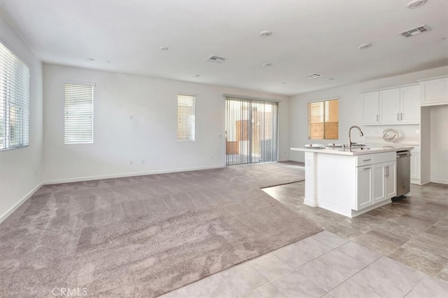 kitchen with white cabinets, sink, light colored carpet, and an island with sink