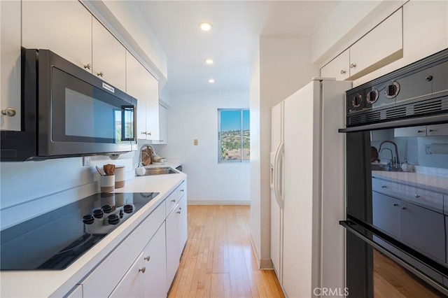 kitchen featuring sink, white cabinets, light wood-type flooring, and black appliances