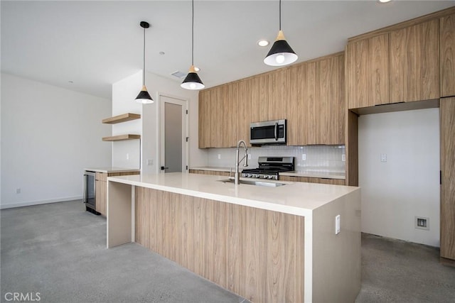 kitchen with sink, stainless steel appliances, hanging light fixtures, and an island with sink