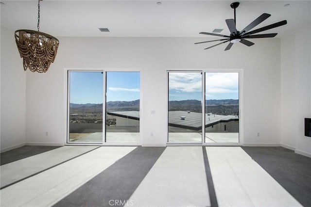 carpeted empty room featuring ceiling fan with notable chandelier, a healthy amount of sunlight, and a mountain view