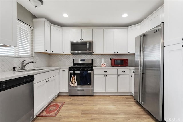 kitchen featuring white cabinetry, sink, stainless steel appliances, light hardwood / wood-style floors, and decorative backsplash