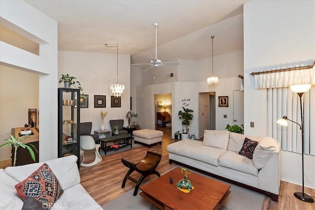 living room with ceiling fan with notable chandelier, wood-type flooring, and high vaulted ceiling