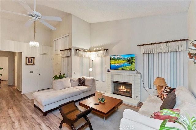 living room featuring a fireplace, light hardwood / wood-style floors, high vaulted ceiling, and ceiling fan